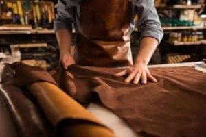 Craftsperson smoothing raw leather hide on workbench – Leather and Kid