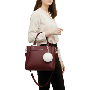 Leather and Kids maroon leather handbag with white pom-pom charm worn on model's shoulder
