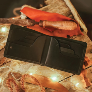 Black Leather Bifold Wallet with Cash Compartment in a leather wallet craft tool styling shot beside a wooden handle awl tool.