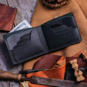 Black Leather Bifold Wallet with Cash Compartment in a leather wallet workshop styled shot surrounded by leathercraft tools and offcuts.