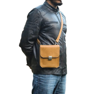 Men's tan leather crossbody sling bag by Leather and Kids worn over shoulder with black jacket