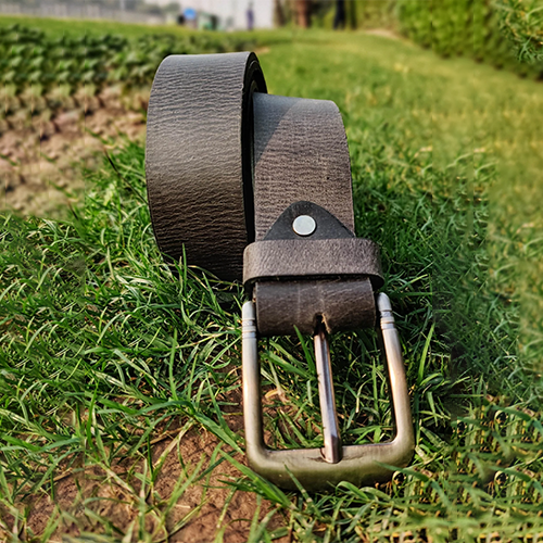 Men's distressed grey-brown leather belt with crackled grain and antique metal pin buckle, rolled up on green grass
