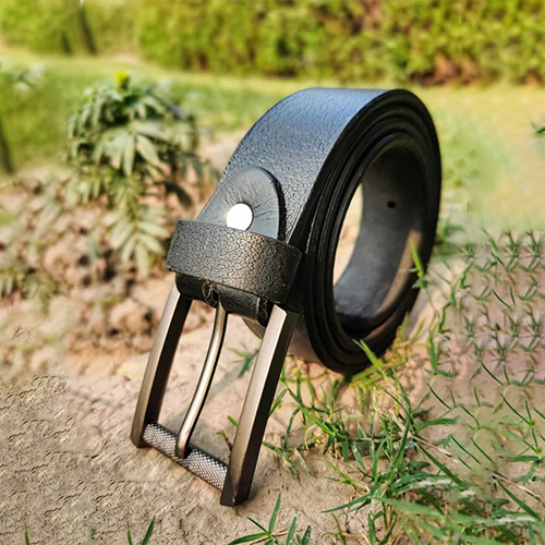 Men's black crackle grain leather belt standing upright on dry ground with green grass, a dark bronze-tone pin buckle with a knurled bottom bar and a silver-tone rivet